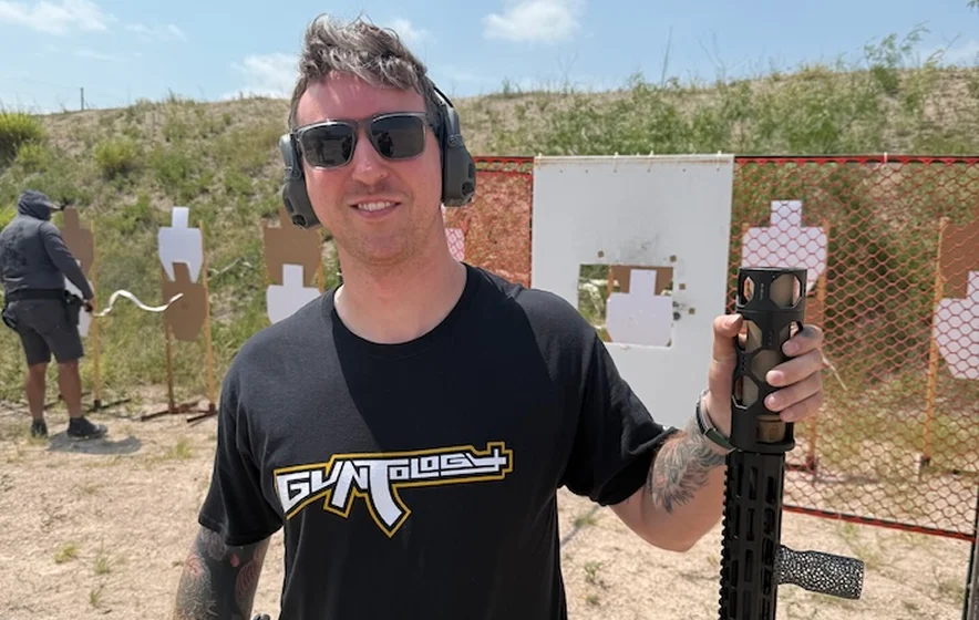 A man grips an AK-47 rifle, positioned in front of a target for shooting practice.
