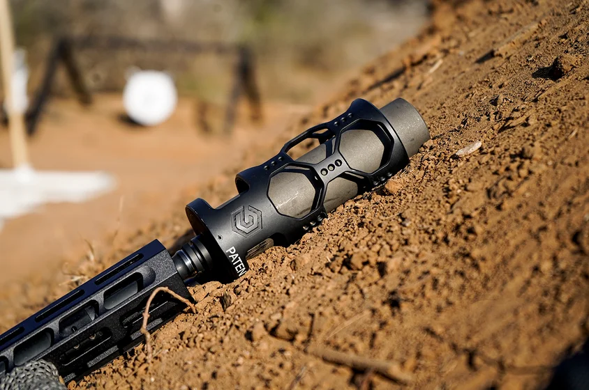 A rifle with a scope rests on the ground, showcasing its sleek design and precision features.