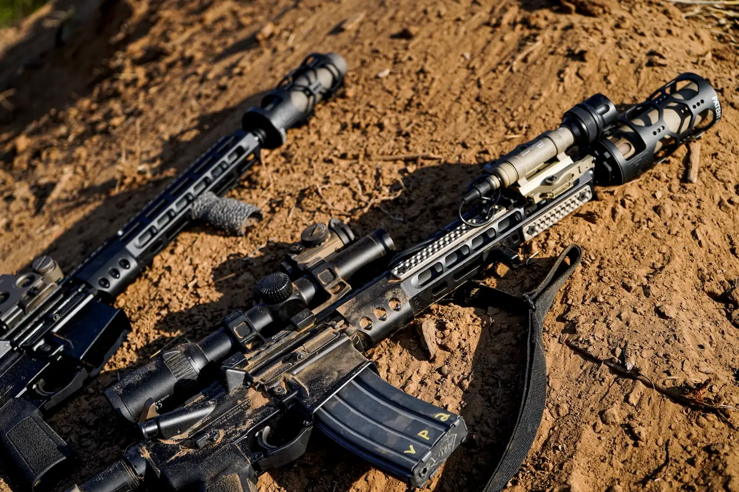 Two rifles resting on the ground, partially buried in dirt, with a natural outdoor setting in the background.