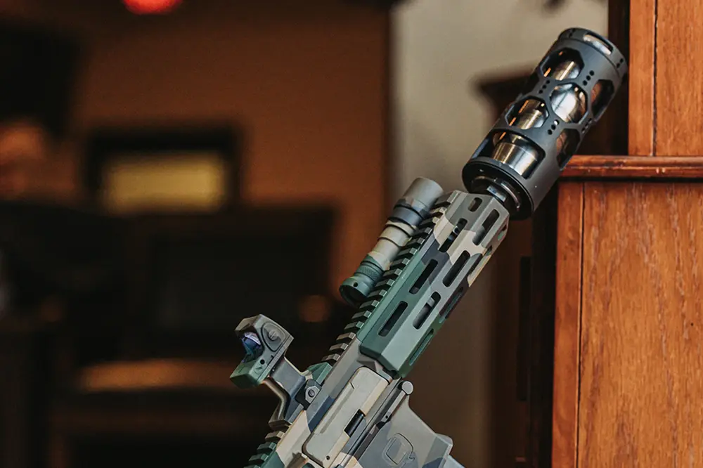 A rifle is positioned on a wooden table, emphasizing the craftsmanship of both the weapon and the rifle suppressor.