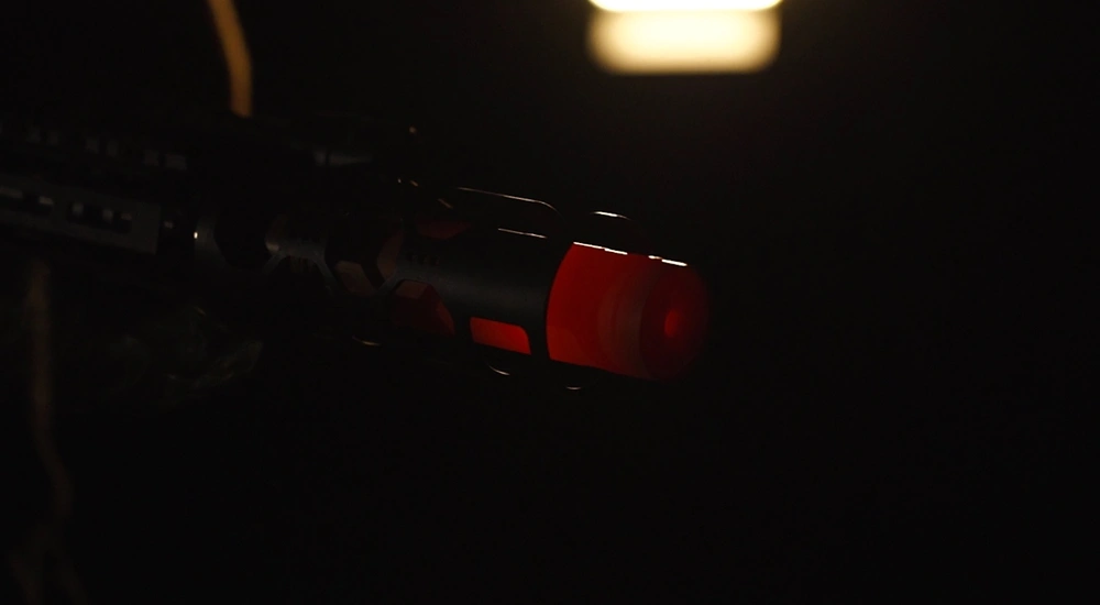 A person holding a gun in a dark environment, emphasizing the heat of the suppressor.