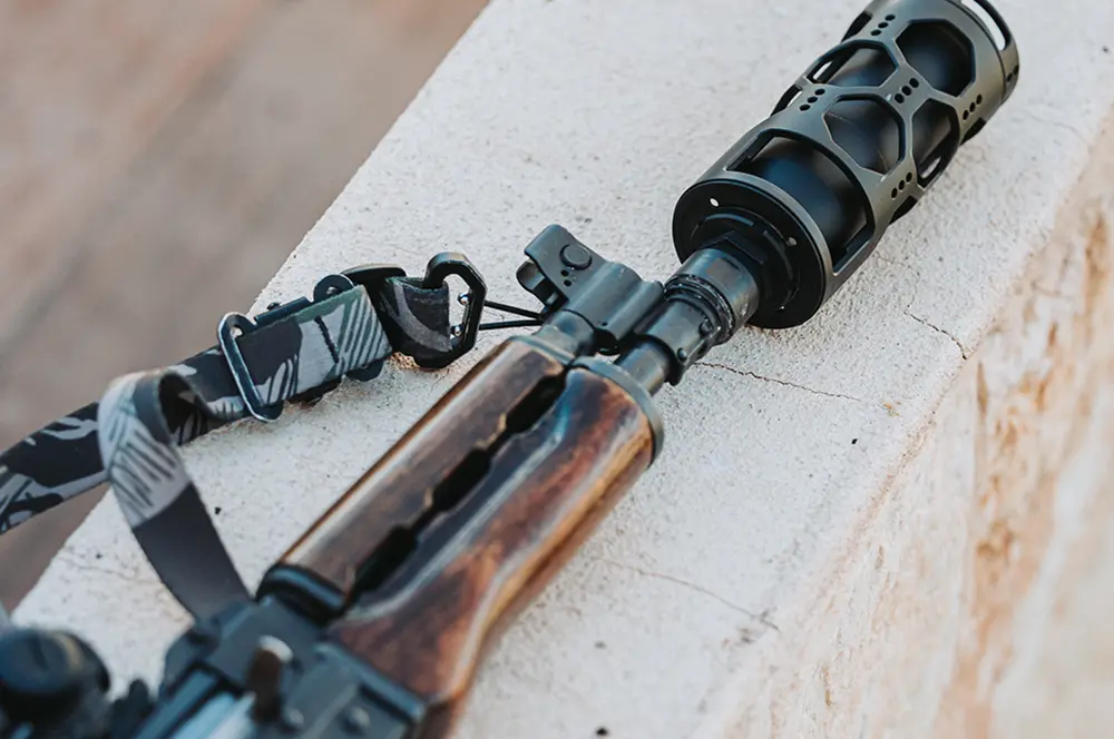 Rifle with a scope and suppressor, resting on a wall, showcasing heat protection features.