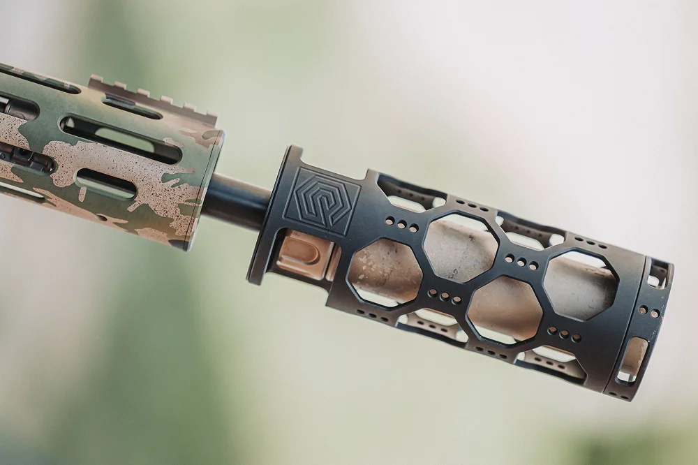Close-up of a camo-patterned rifle featuring a suppressor with heat protection.